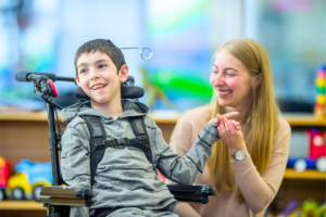 young boy in a wheelchair smiling with his female caregiver
