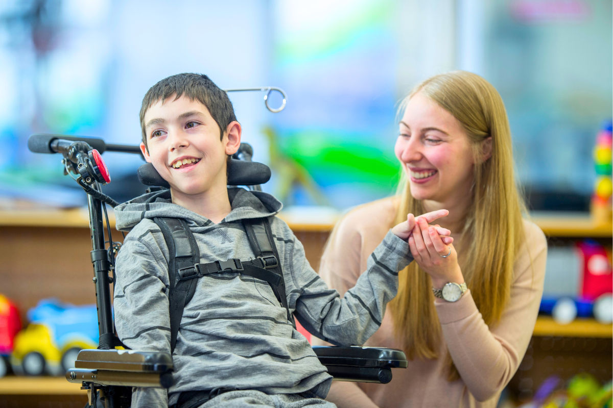 young boy in a wheelchair smiling with his female caregiver