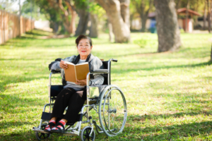 a woman sitting in a wheelchair reading a book outside in a green park