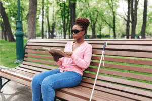 a woman who is blind reads a braille book on a park bench